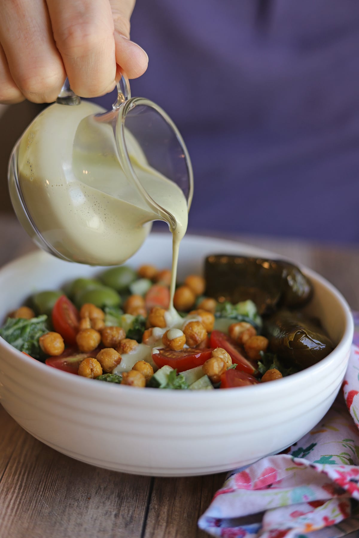 Creamy cashew-based dressing being poured onto kale salad with roasted chickpeas and dolmas.