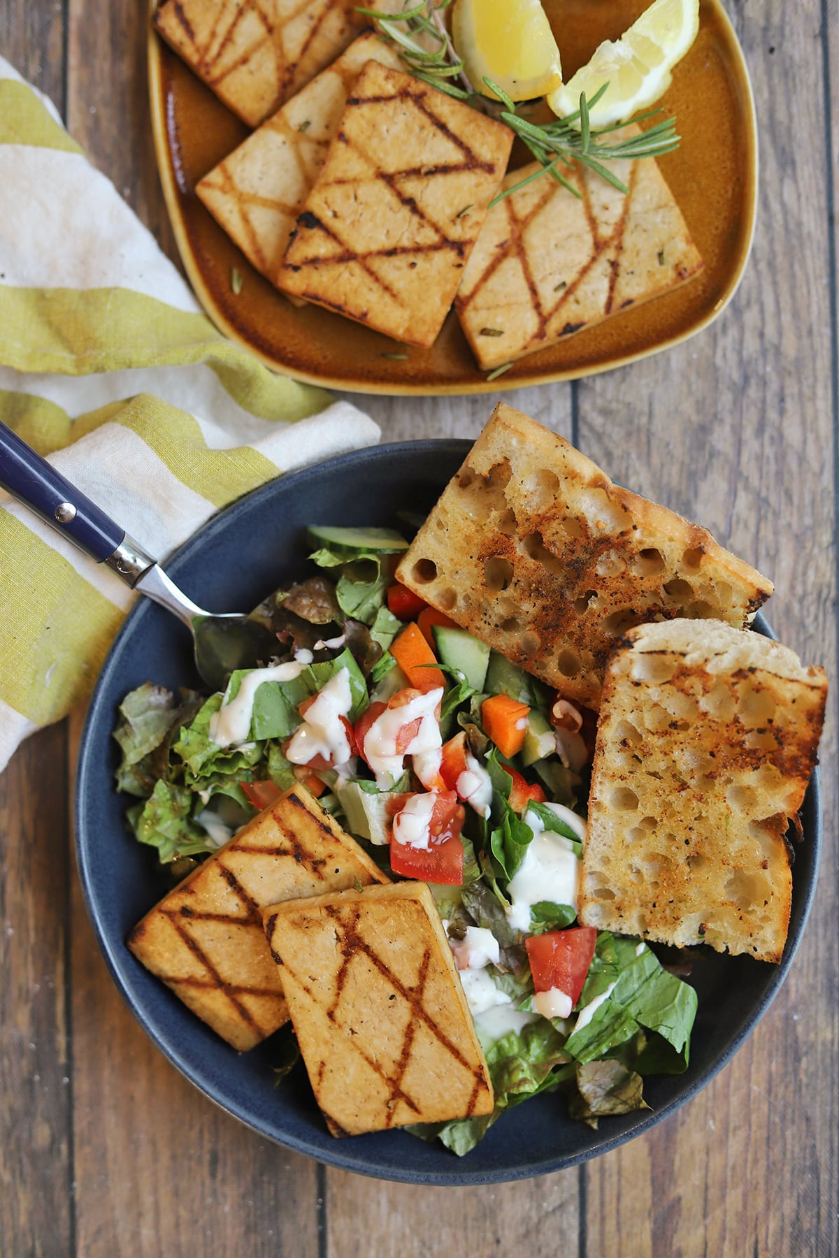 Grilled tofu in bowl with salad covered in creamy dressing and garlic bread.
