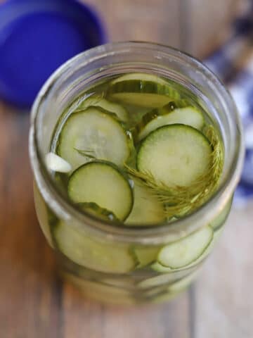 Crisp slices of cucumber in jar with brine, fresh dill, and slivered garlic.