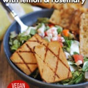 Text overlay: Grilled tofu with lemon & rosemary, vegan cookout recipe, cadryskitchen.com. Slabs of grilled tofu on plate with salad and garlic bread.