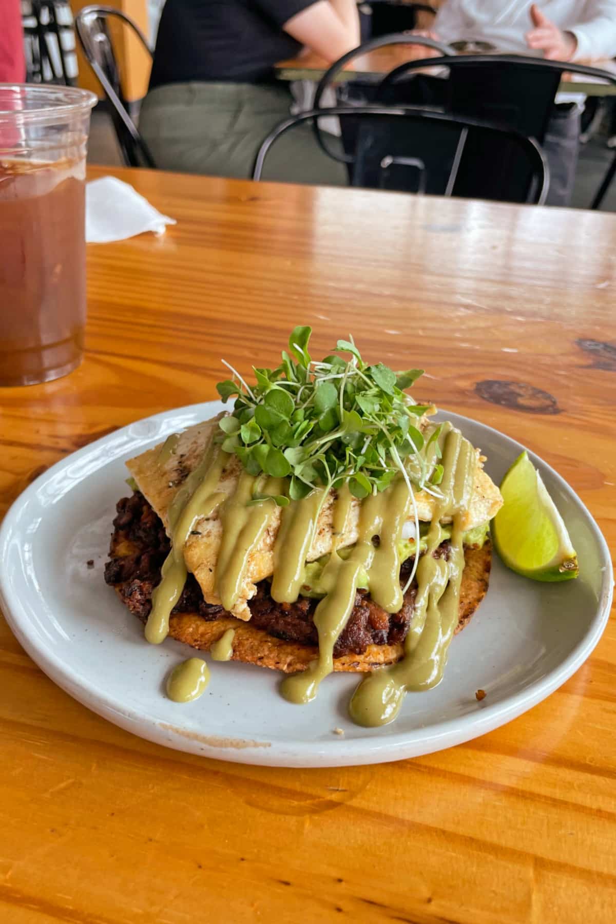 Vegan tostada with black beans, avocado sauce, micro greens, and vegan egg on plate with lime wedge.