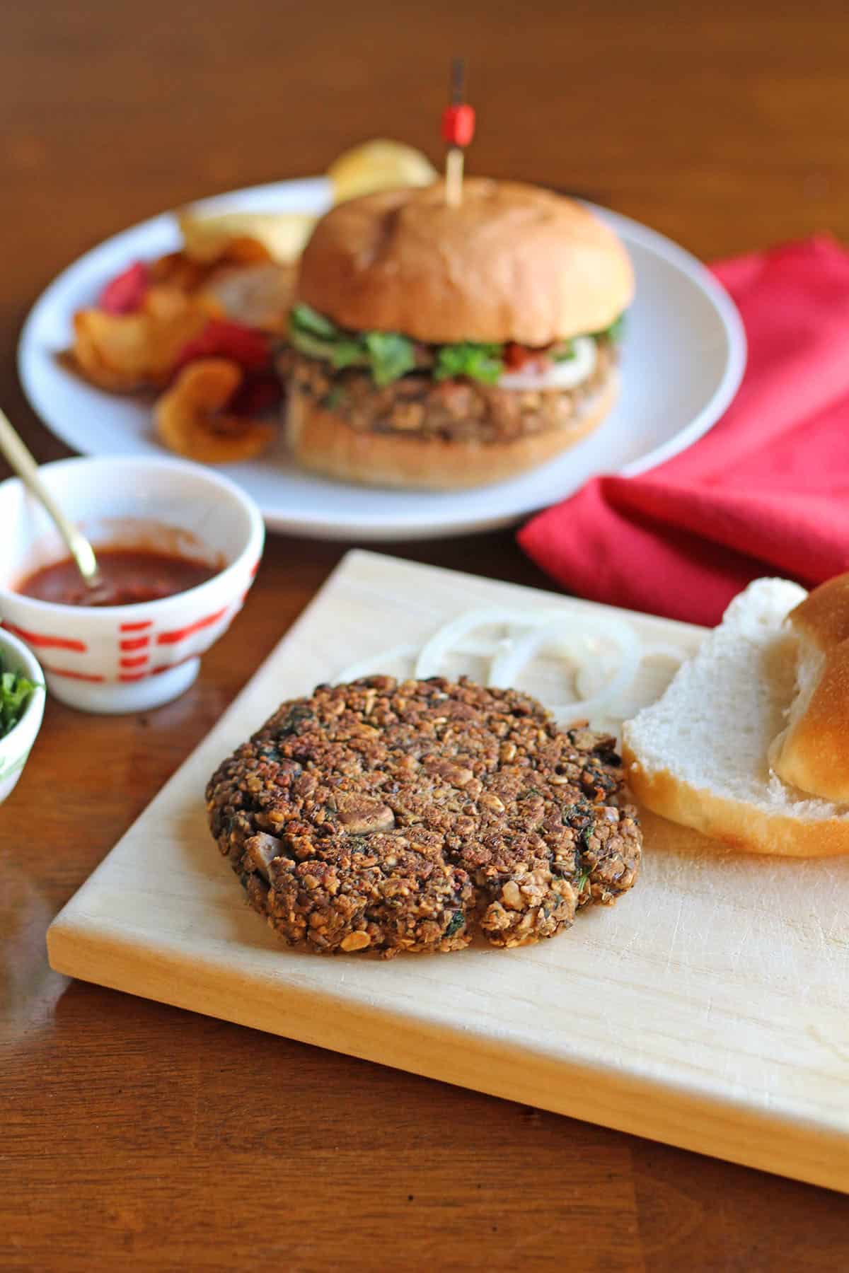 Lentil burger patty on cutting board with onions, bun, and pasta sauce.