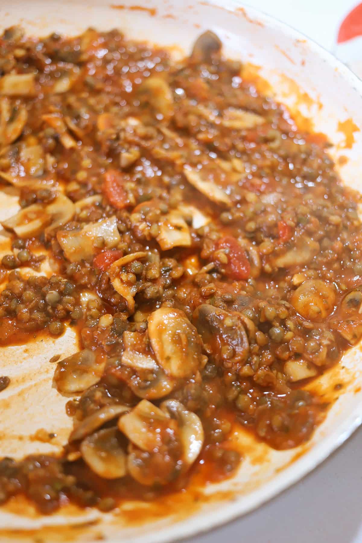 Lentils in pasta sauce with mushrooms in pan.