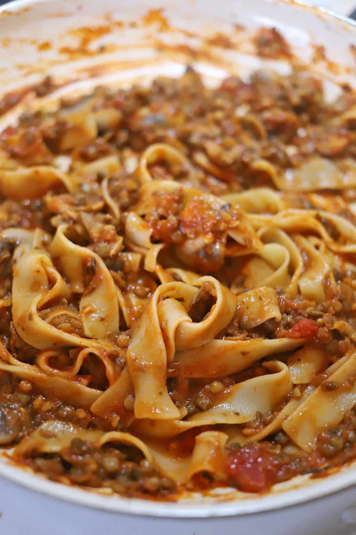 Close-up long noodles in pan, tossed with lentils and pasta sauce.