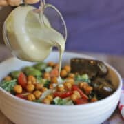 Creamy vegan dressing being poured onto salad with roasted chickpeas and dolmas.