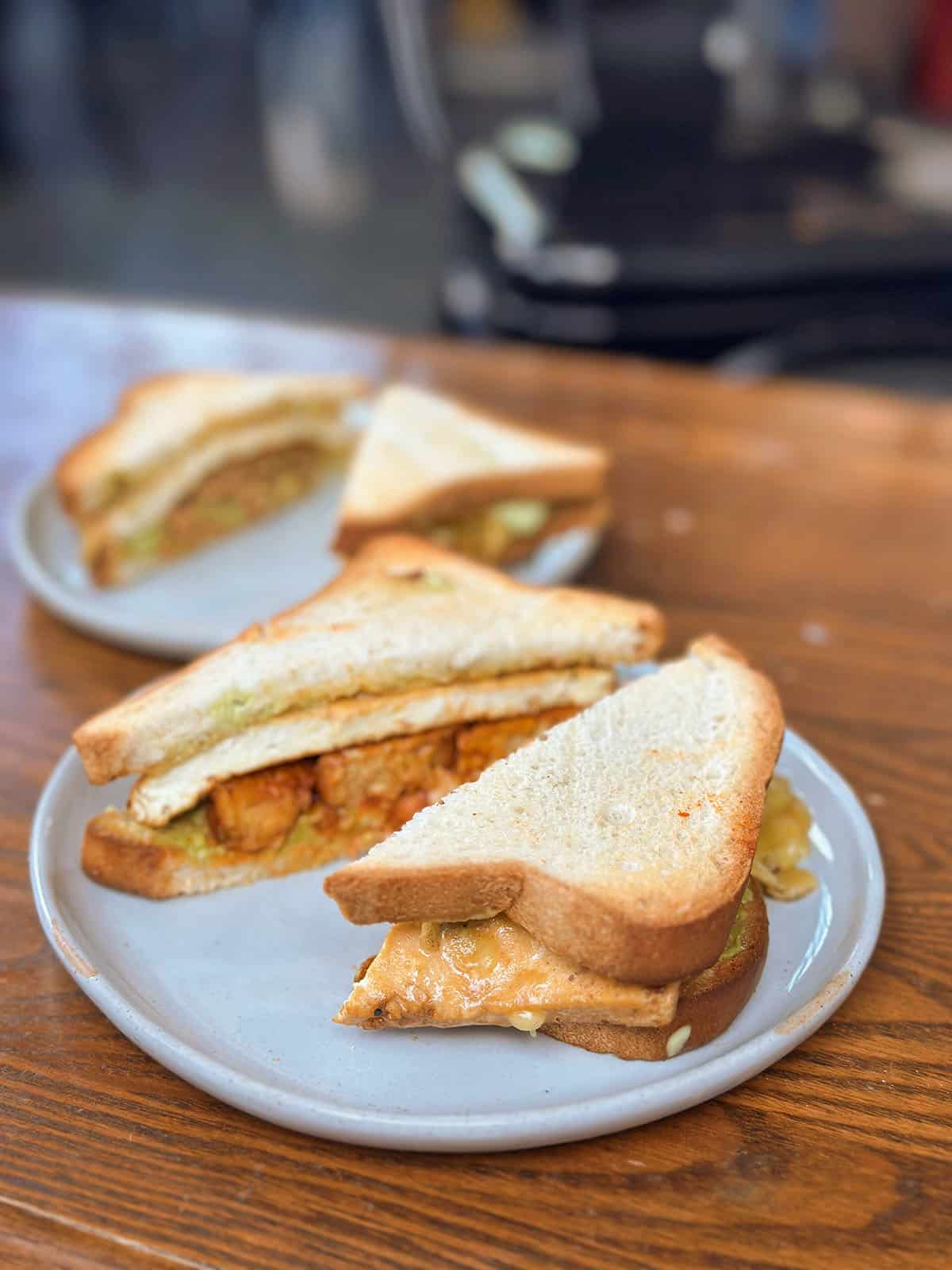 Breakfast sandwich on white bread with tofu, tempeh bacon, vegan cheese, and avocado.