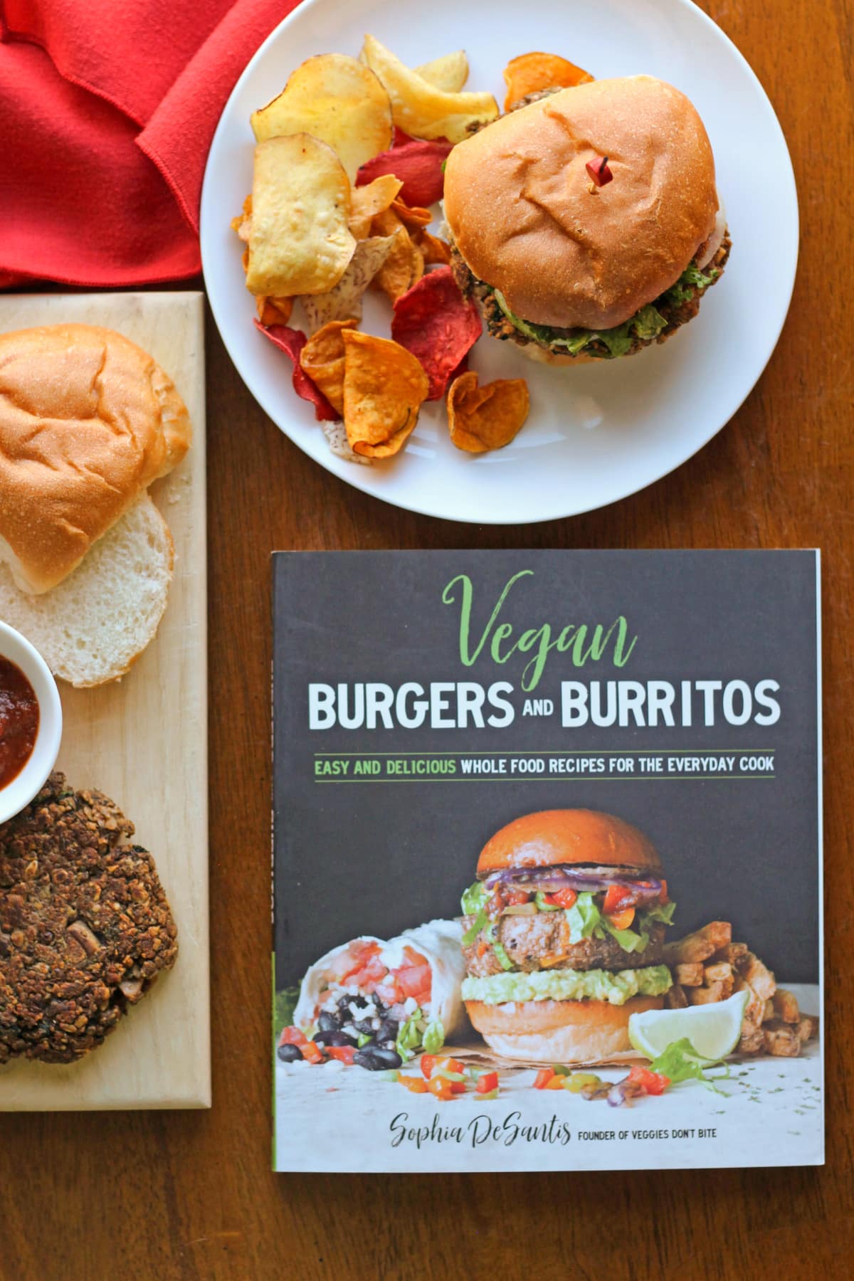 Vegan Burgers and Burritos cookbook on table by lentil burgers and chips.