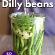 Text overlay: Dilly beans, quick pickled green beans, cadryskitchen.com. Pickling brine being poured over fresh green beans.