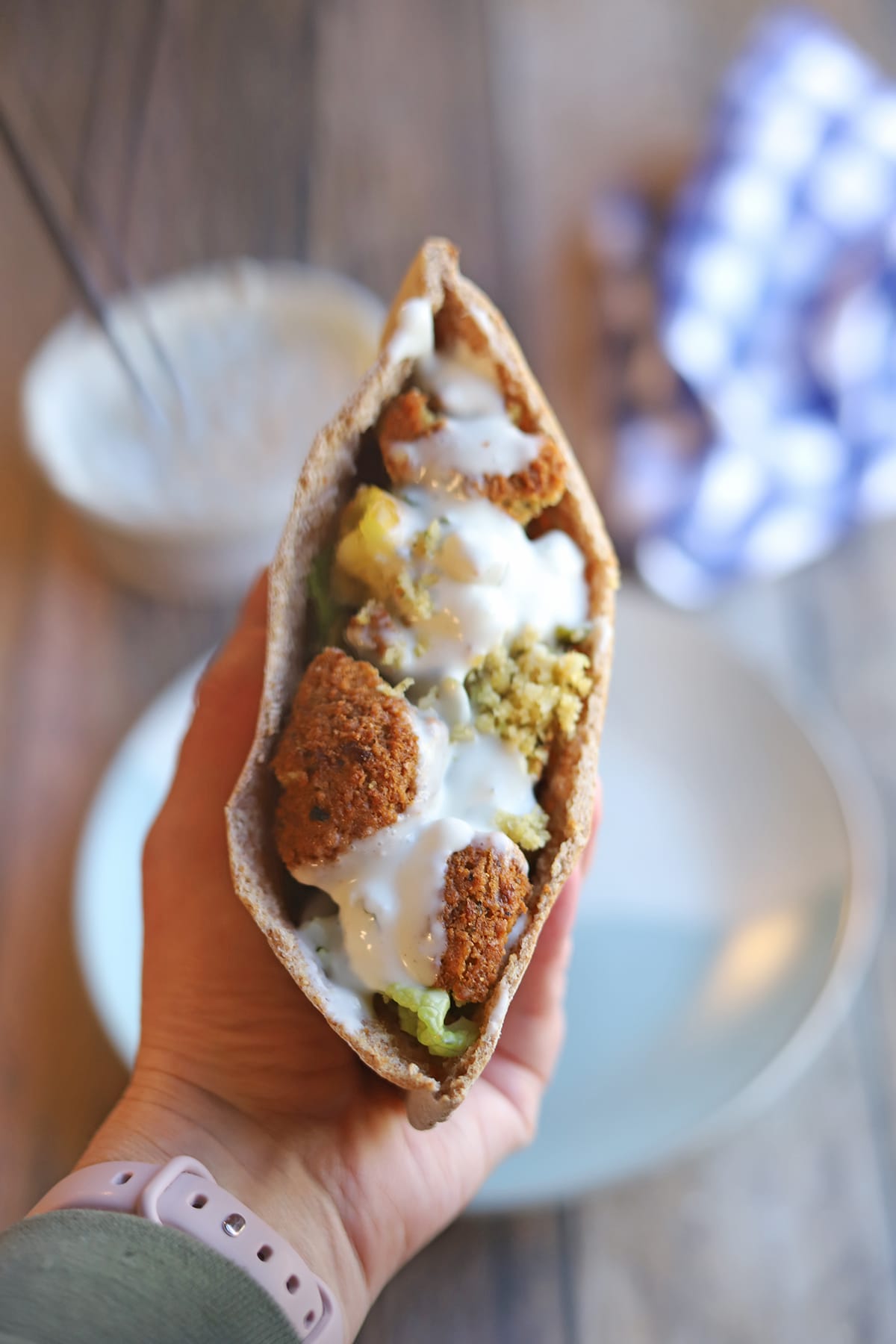Hand holding falafel pita pocket topped with Trader Joe's vegan tzatziki.