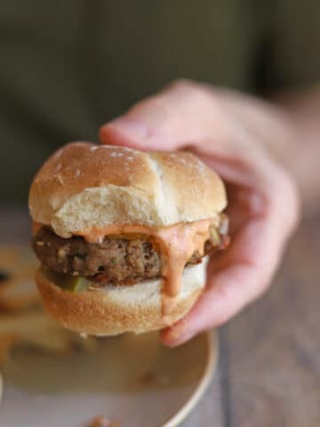 Hand holding veggie burger with vegan Big Mac sauce topping.