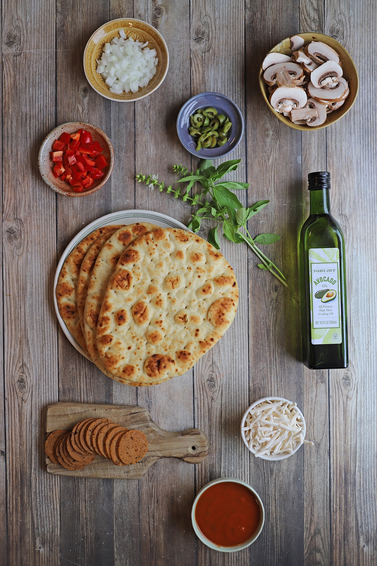 Ingredients for flatbread pizza with garlic naan, veggies, oil, vegan cheese, and marinara.