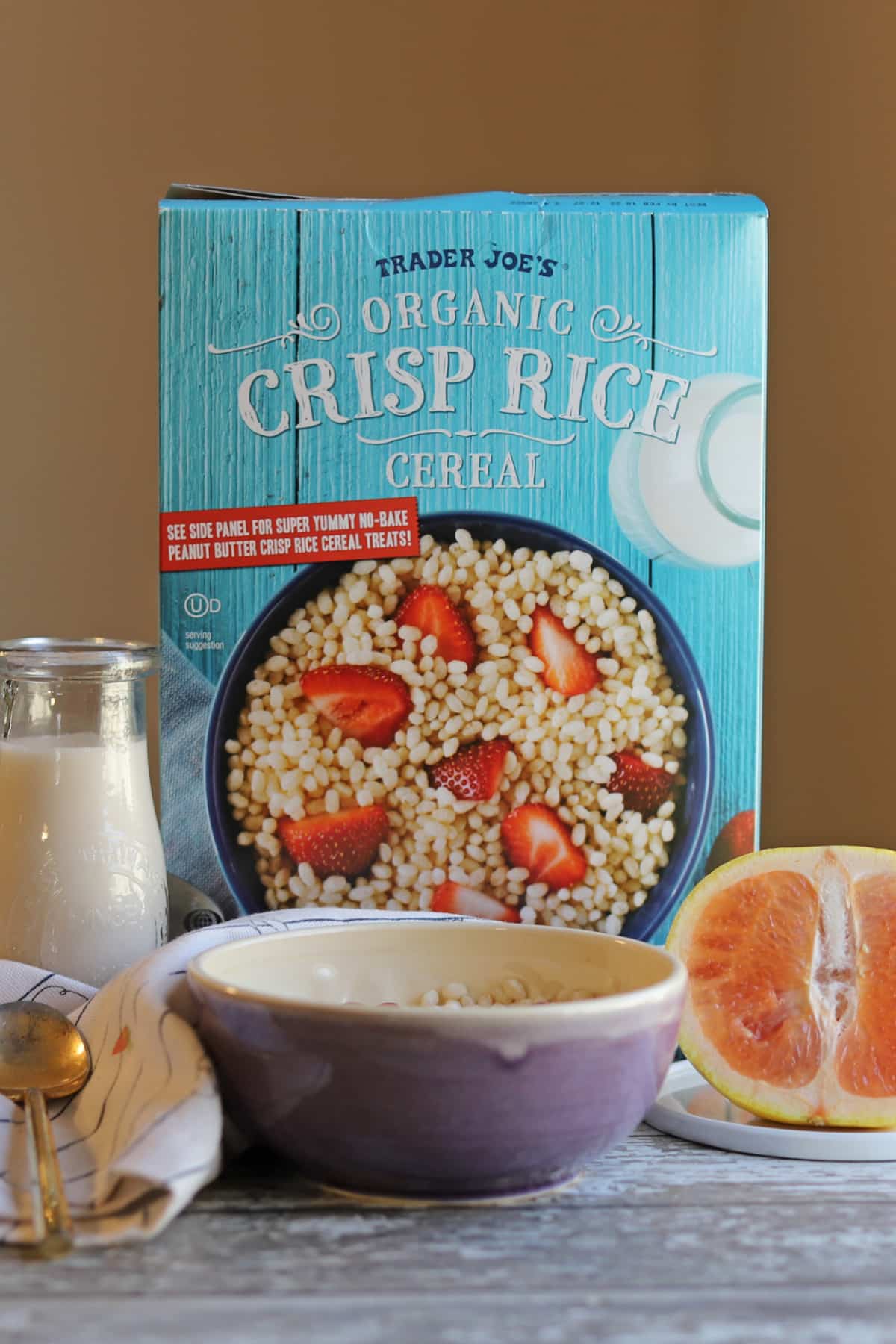 Box of Trader Joe's organic Crisp Rice Cereal on table with bowl, non-dairy milk, spoon, and grapefruit.