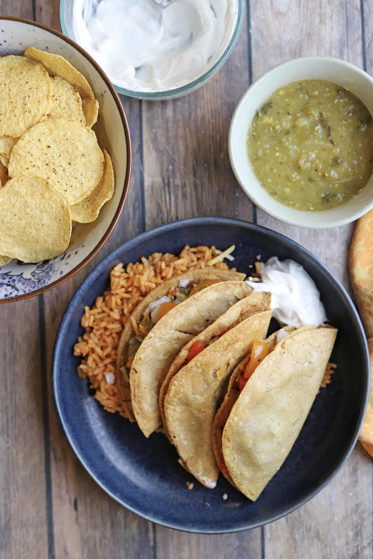 Trader Joe's potato tacos on plate with Spanish style rice, vegan sour cream, salsa verde, and tortilla chips.