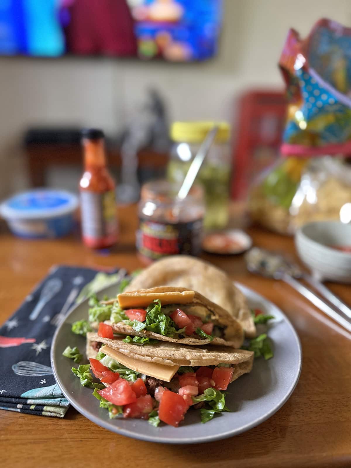 Trader Joe's potato tacos stuffed with tomatoes, vegan cheddar cheese slice, and lettuce on plate.