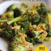 Text overlay: Roasted broccoli with chili crisp sauce, bold umami flavor, cadryskitchen.com. Broccoli side dish on plate.