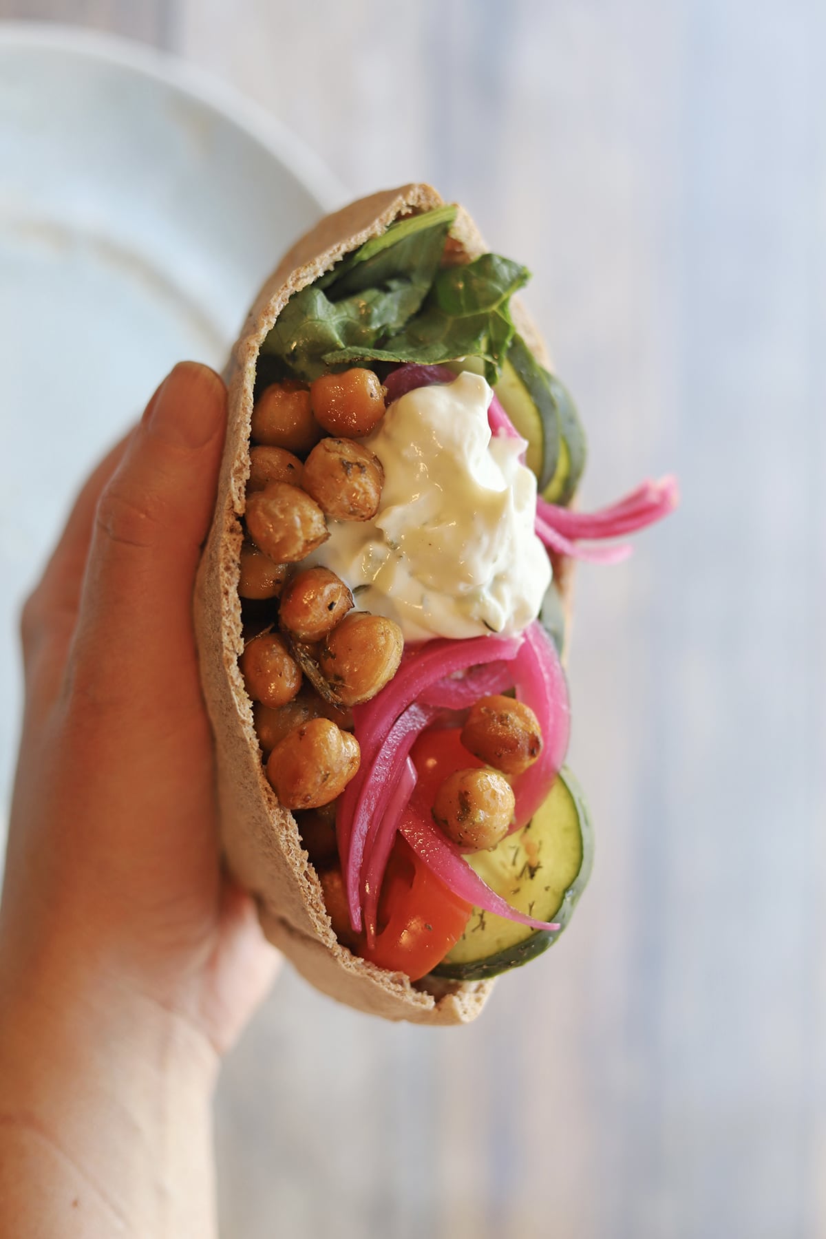 Hand holding pita pocket stuffed with roasted chickpeas, lettuce, cucumber, and pickled red onions.