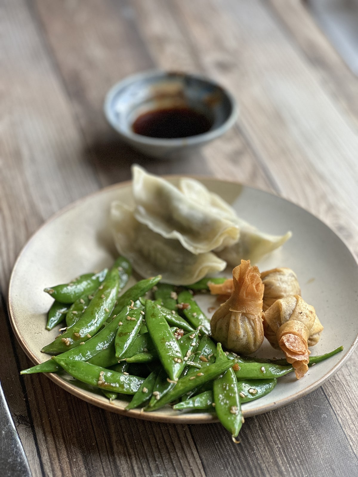 Thai vegetable gyoza with dipping sauce, vegetable pouches, and stir-fried sugar snap peas on plate.