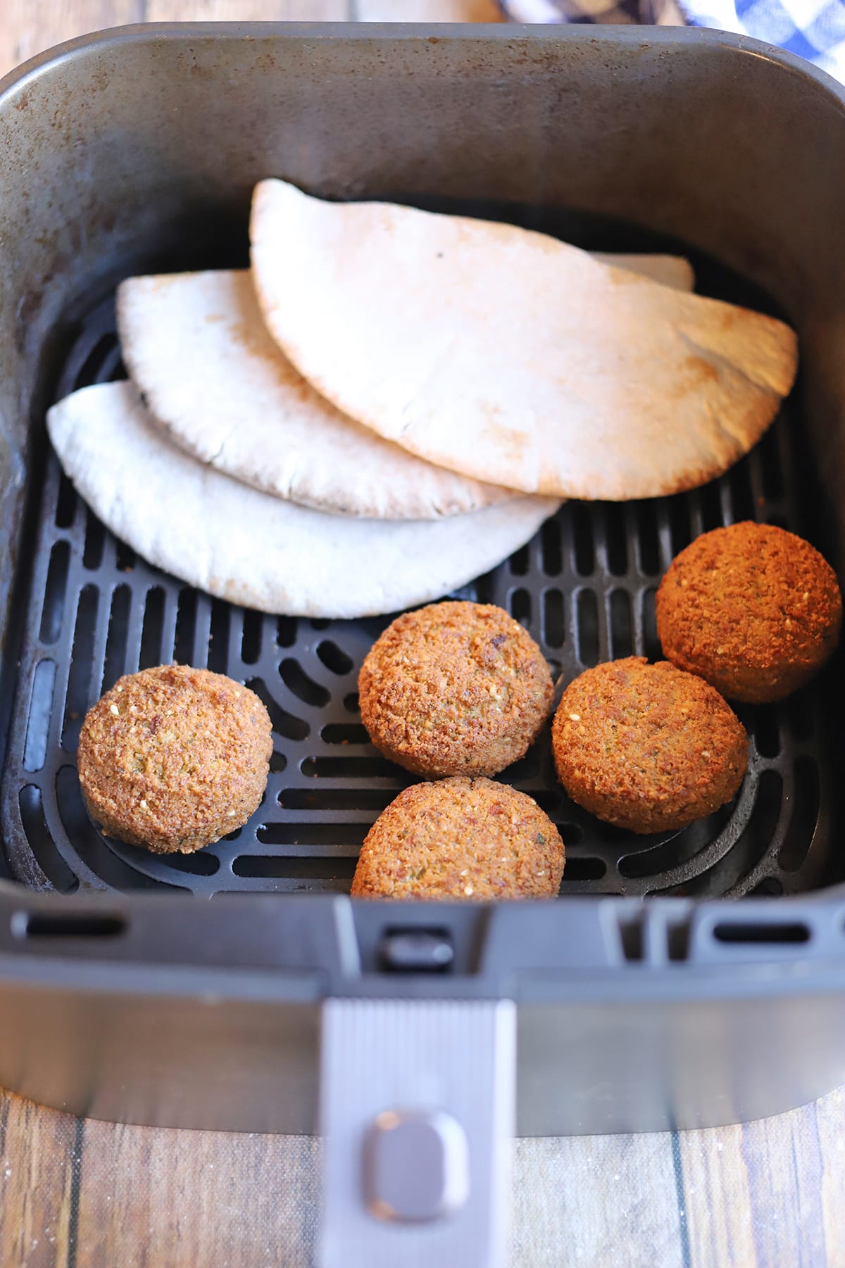Falafel and pita halves in air fryer basket.