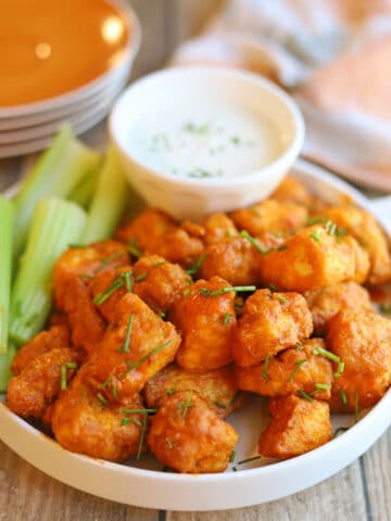 Platter of vegan buffalo tofu bites with celery sticks and dairy-free dressing for dipping.