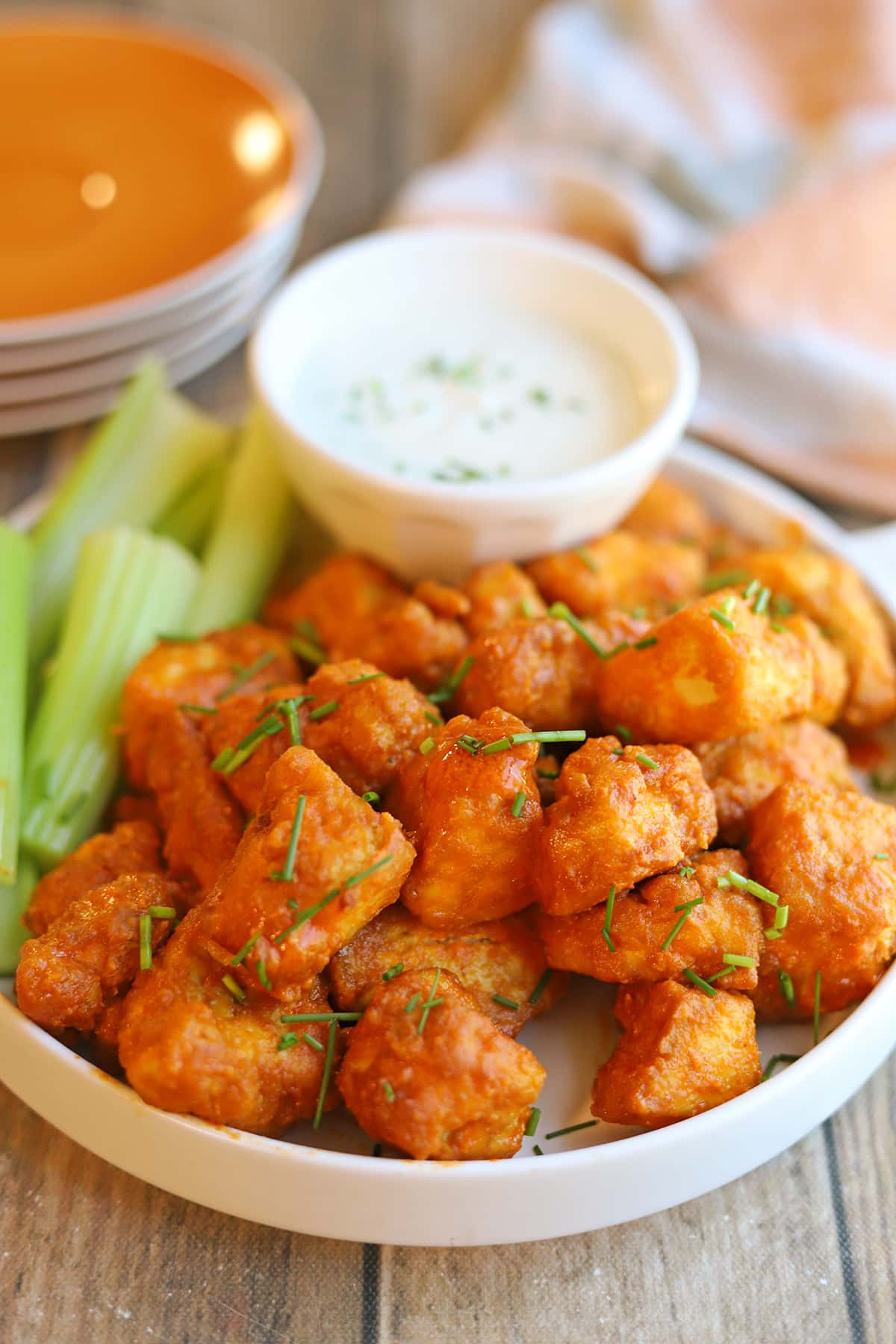 Platter of vegan buffalo tofu bites with celery sticks and dairy-free dressing for dipping.