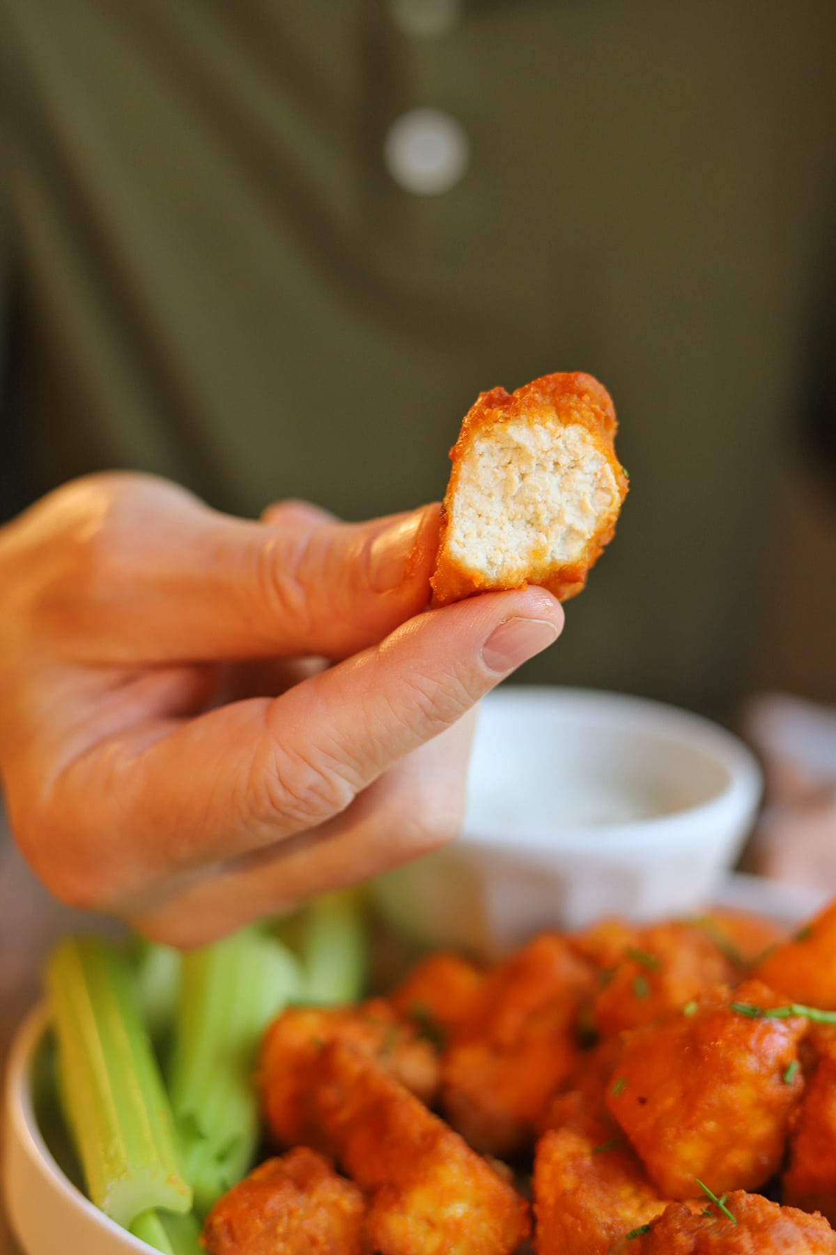 Hand holding bitten vegan buffalo tofu with saucy edges and white middle.