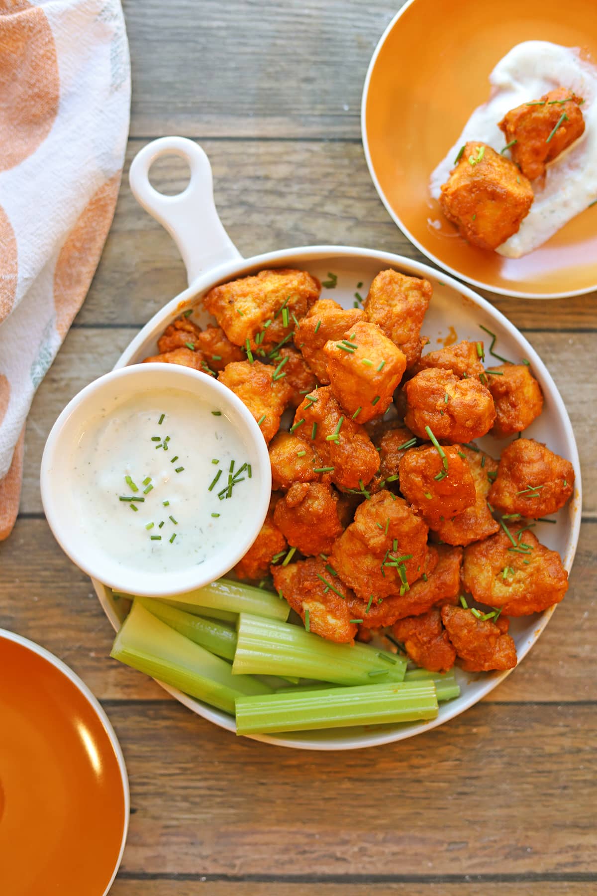Vegan buffalo bites appetizer on table with appetizer plates, celery, and onion garlic dressing.