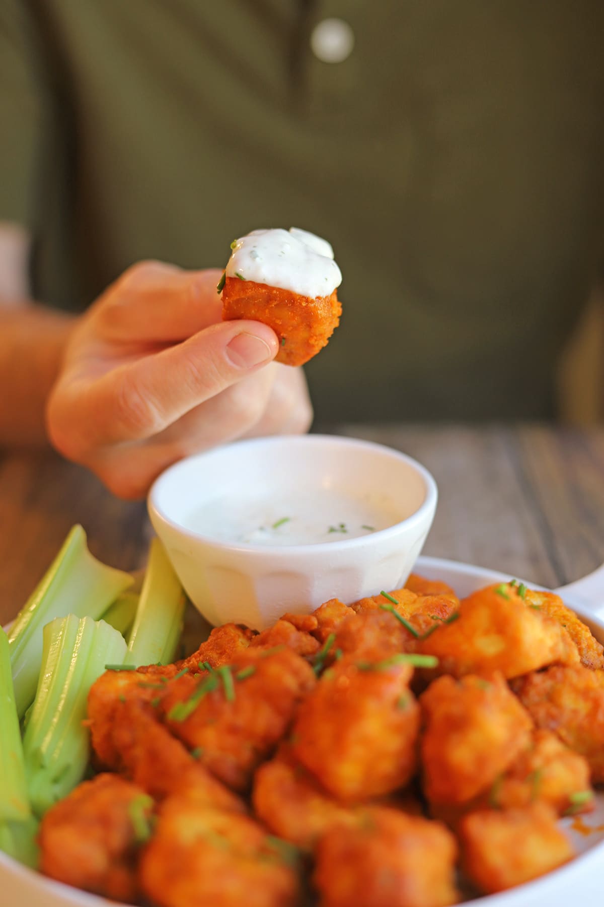 Hand holding vegan buffalo wing dunked in onion and garlic dressing.