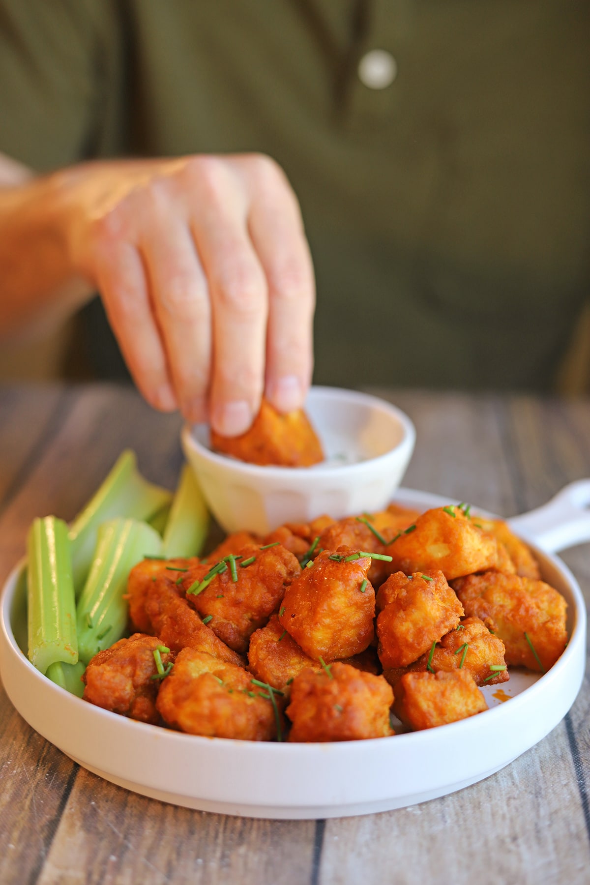 Hand dunking vegan buffalo wing into dipping sauce on platter.