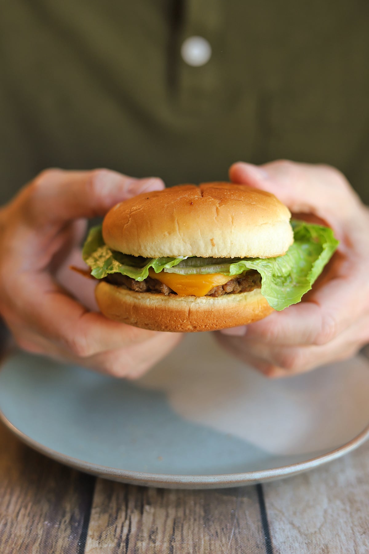 Hands holding vegan cheeseburger with pickles, onions, and lettuce.