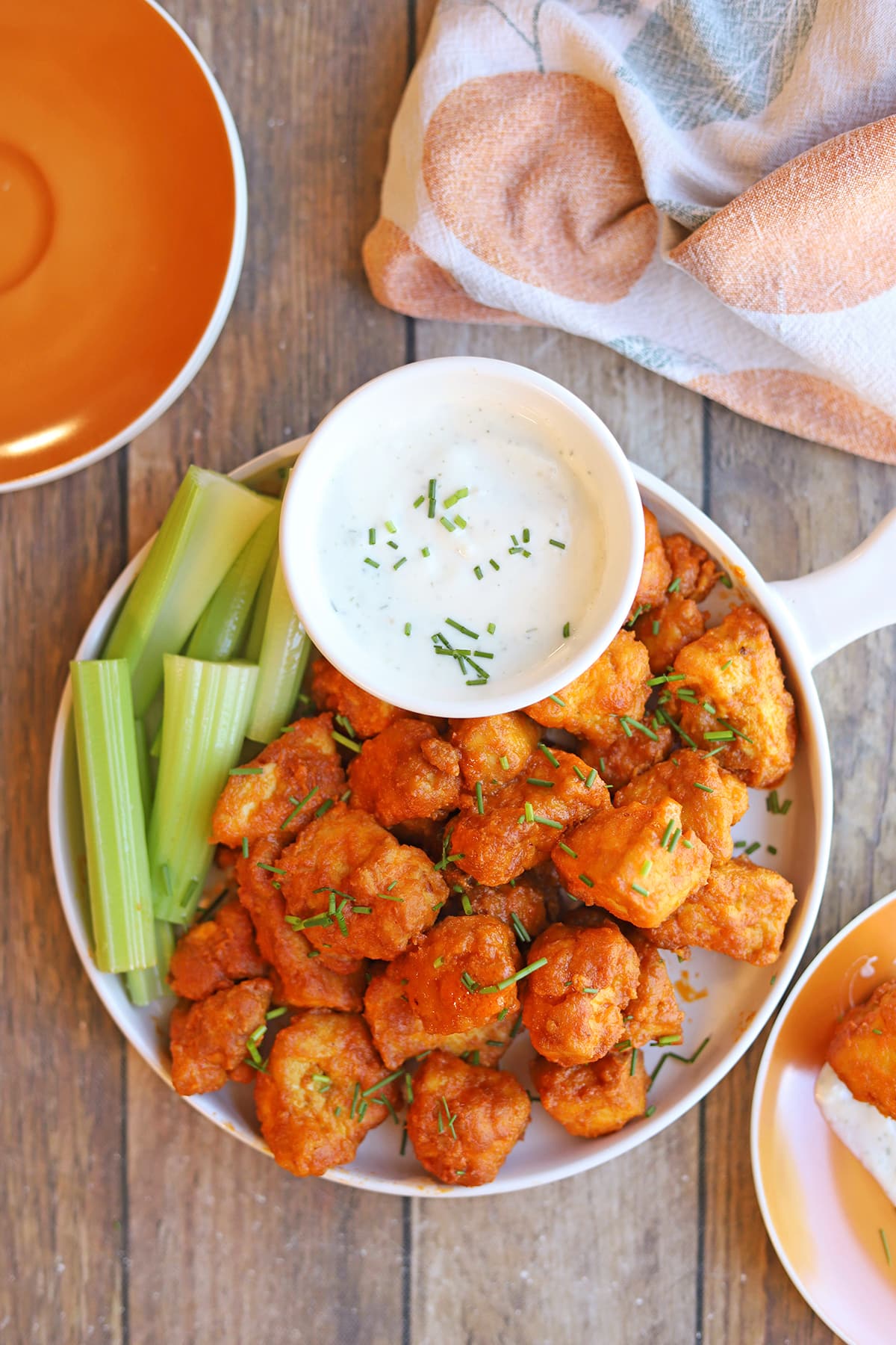 Spicy buffalo tofu bites with onion and garlic dressing, celery sticks, and appetizer plates.