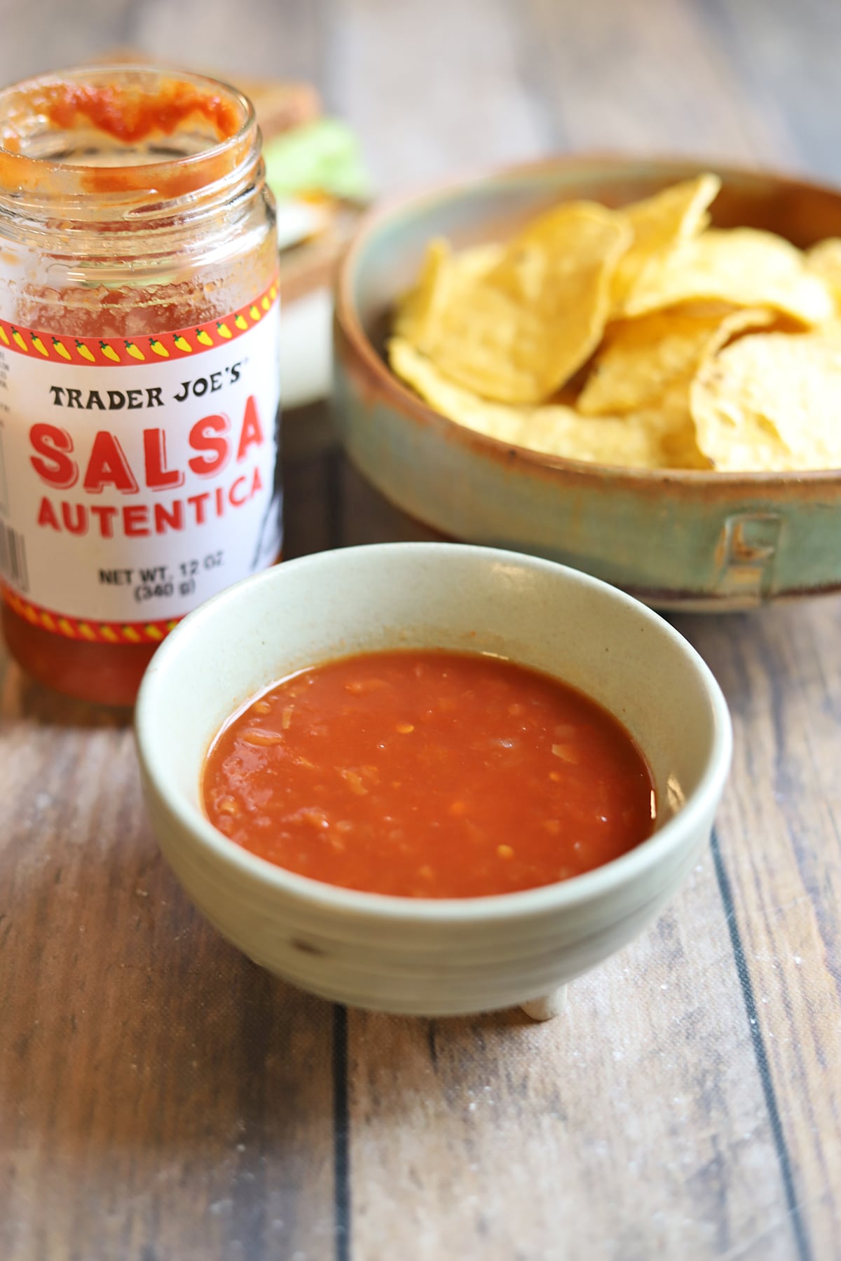 Bottle of salsa autentica by bowl of sauce and tortilla chips.