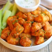 Crispy buffalo tofu bites on platter with celery sticks and dipping sauce.