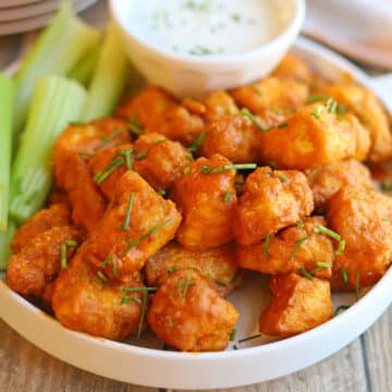 Crispy buffalo tofu bites on platter with celery sticks and dipping sauce.