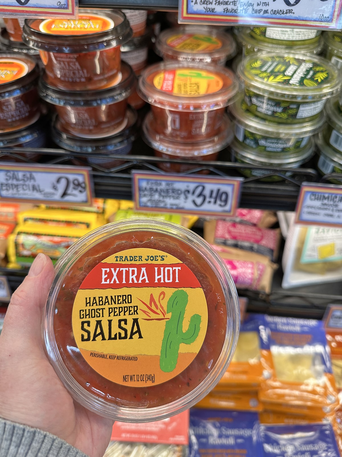 Hand holding container of extra hot habanero ghost pepper salsa at Trader Joe's.