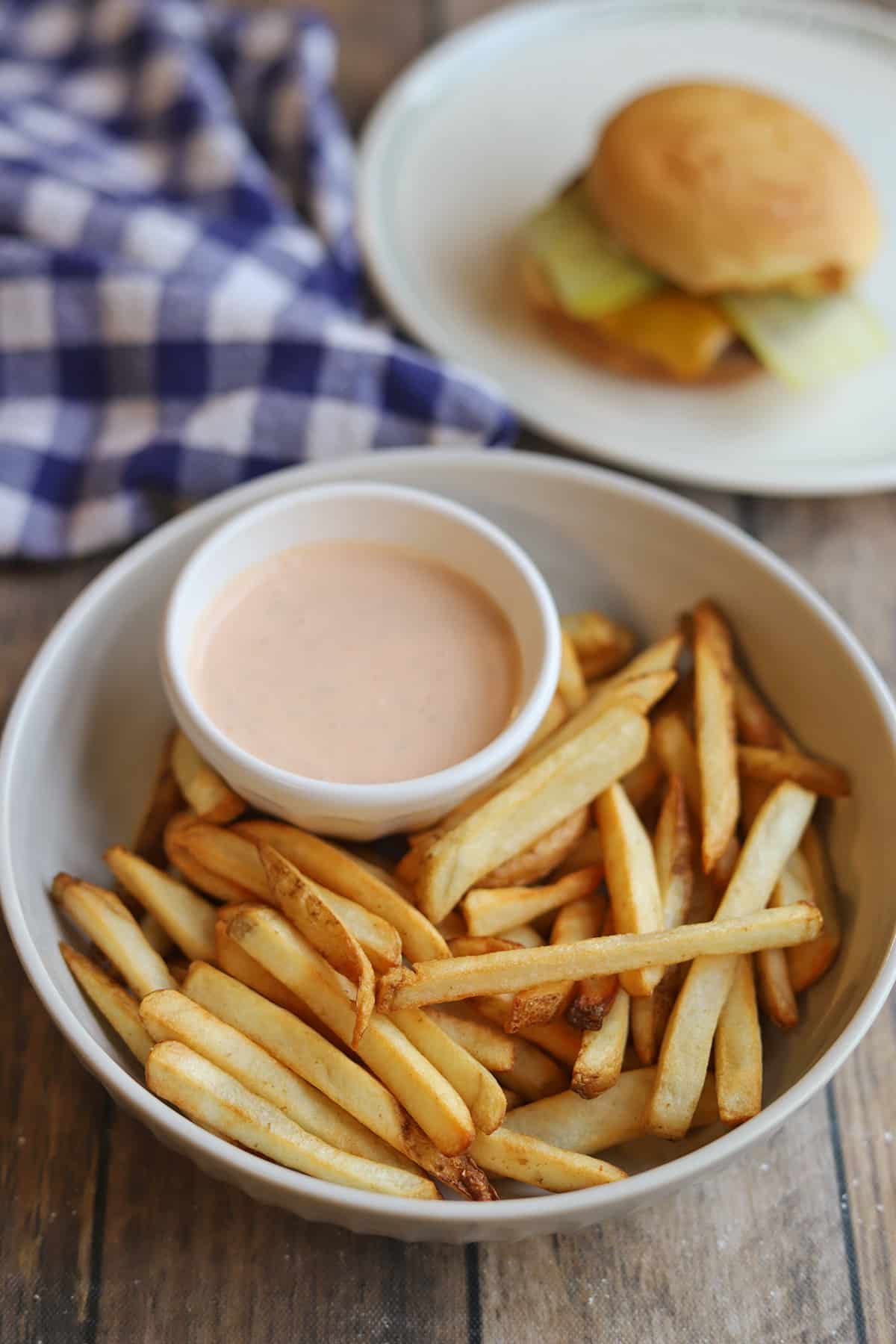 Air fried fries in bowl with vegan Big Mac sauce, vegan cheeseburger in background.