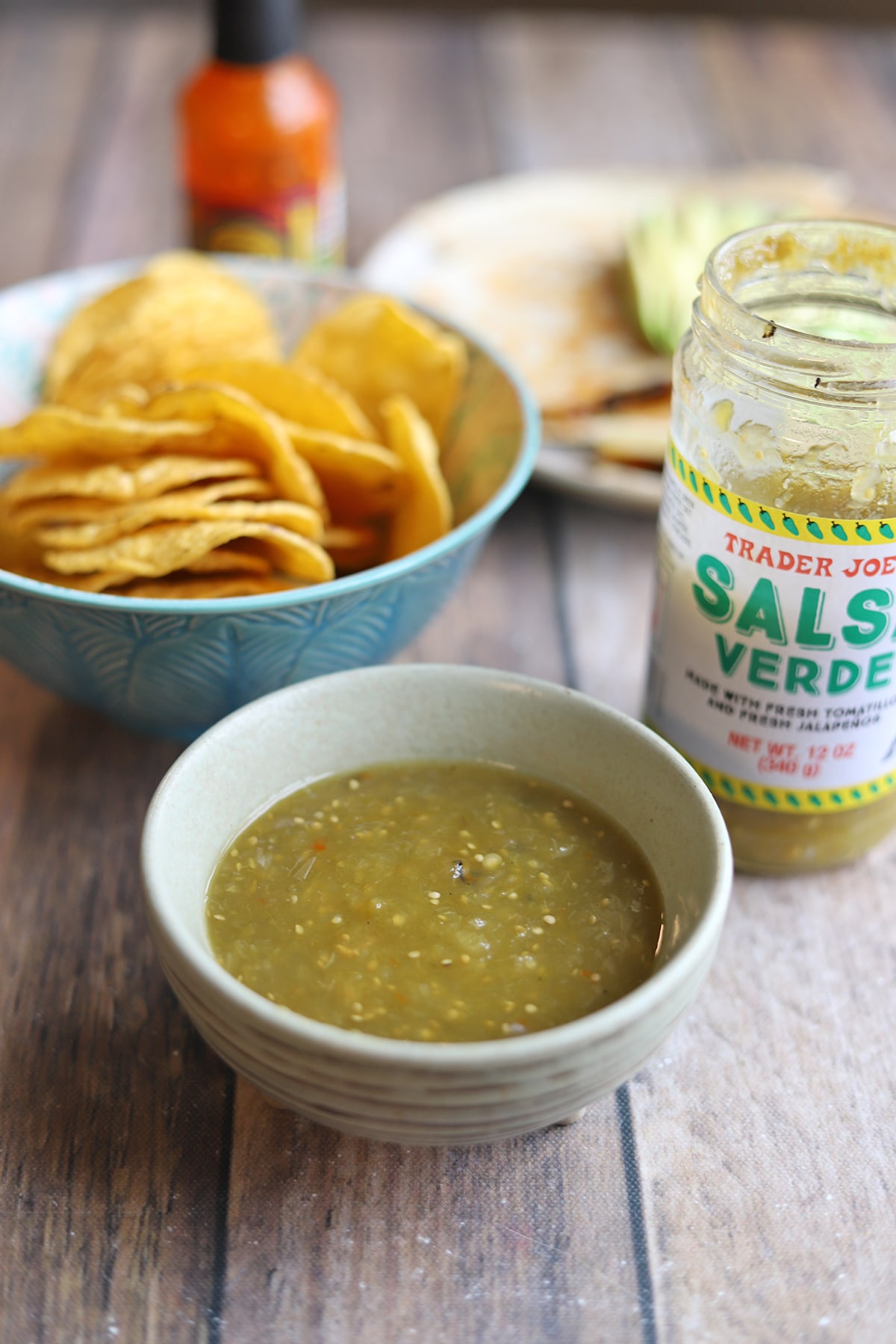 Trader Joe's salsa verde in jar by bowl of green salsa, tortilla chips, and a vegan quesadilla.
