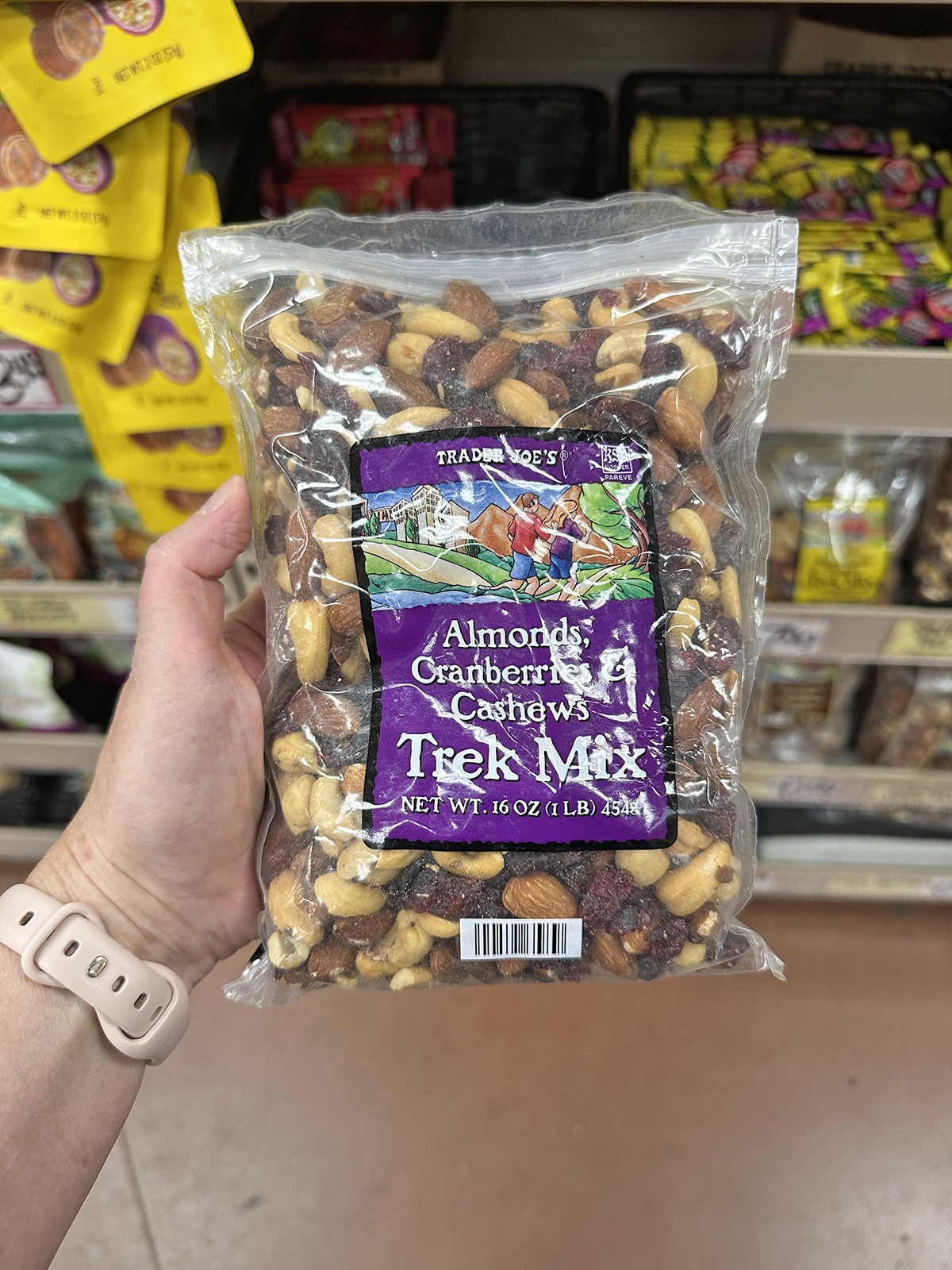 Hand holdign package of almonds, cranberries, and cashews trek mix.