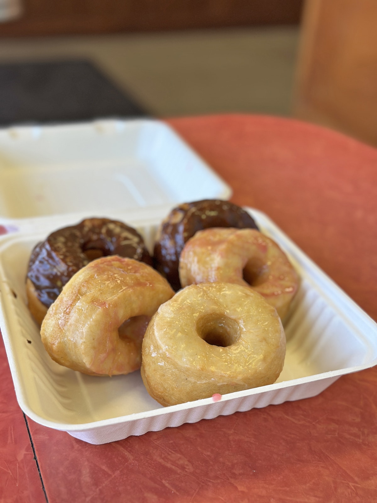 Puffy glazed donuts in to-go container - vanilla, raspberry vanilla, and chocolate.