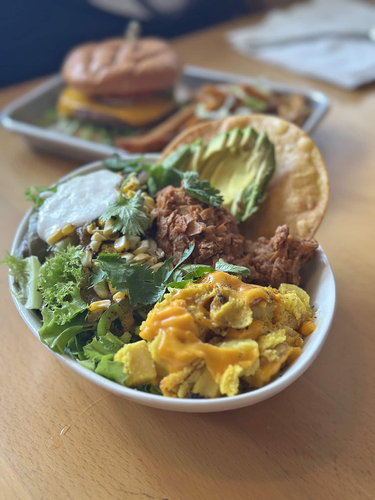 Bowl with corn, black beans, avocado, coconut crusted Lion's Mane mushroom, mung dal vegan egg, vegan cheddar cheese, salsa, mixed greens, house crรจme fraรฎche, lime, cilantro, jalapeรฑo, and a crispy corn tostada.