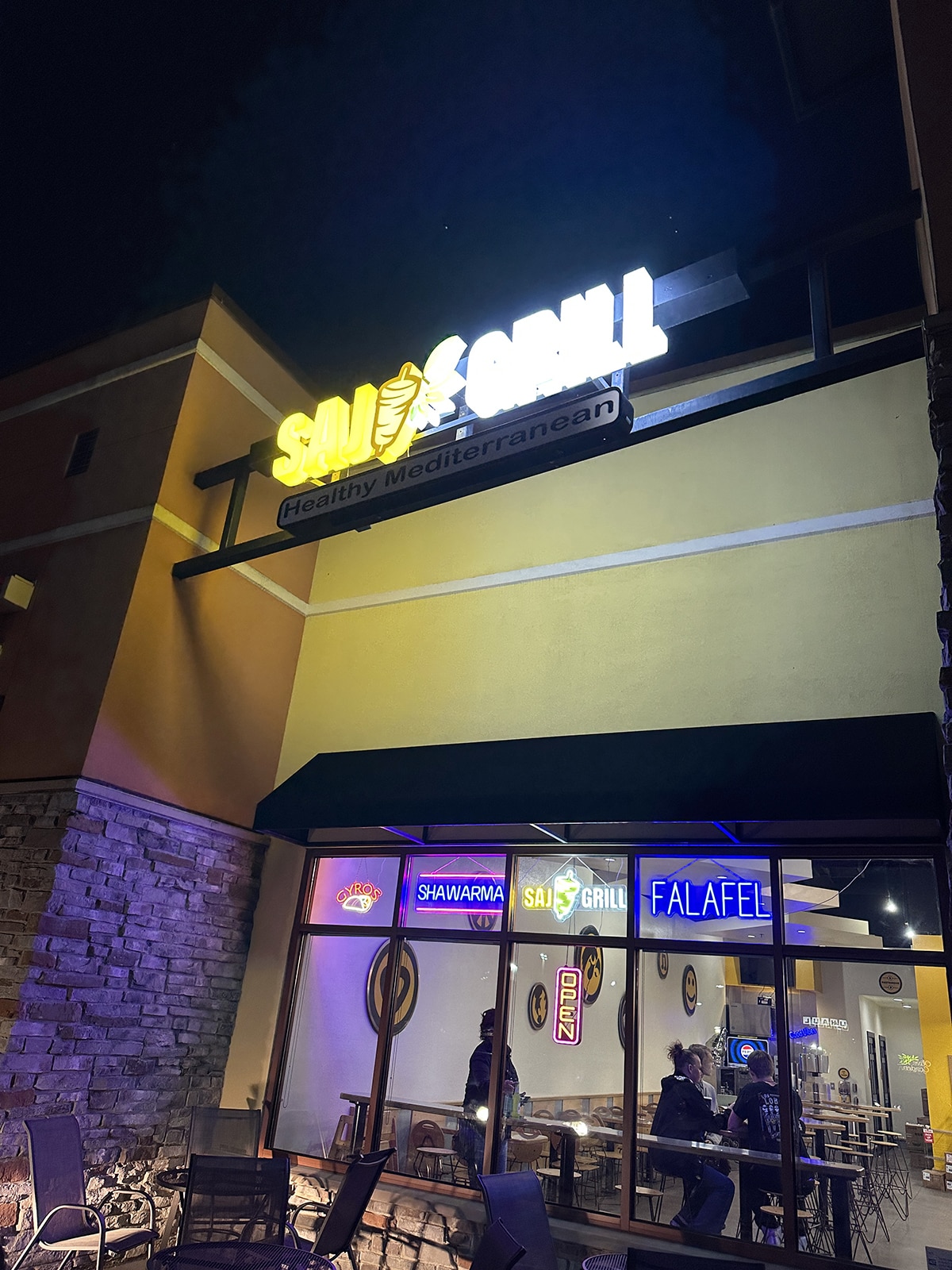Exterior Saj Grill at night with neon signs.