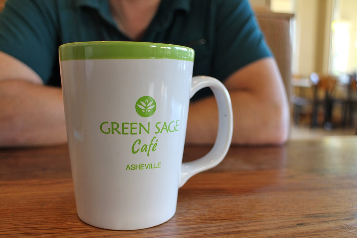 Green Sage Cafe Asheville mug on table.