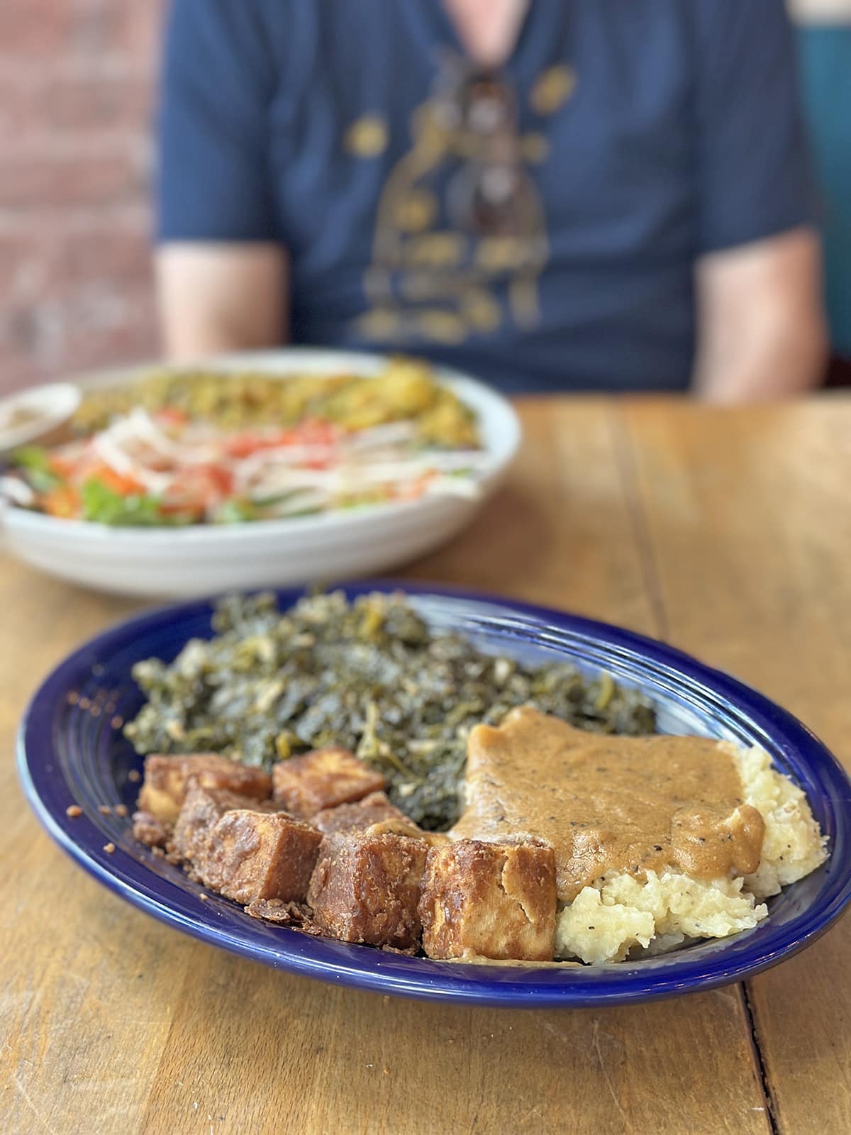 Cubes of peanut butter coated tofu, mashed potatoes and gravy, and collard greens on dark blue plate.