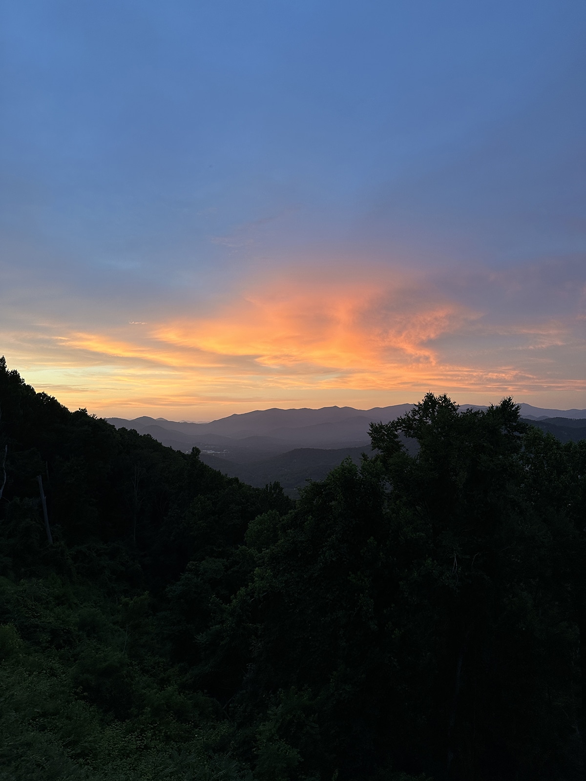 Deep blue sky with pink and yellow clouds over dark Blue Ridge Mountains.