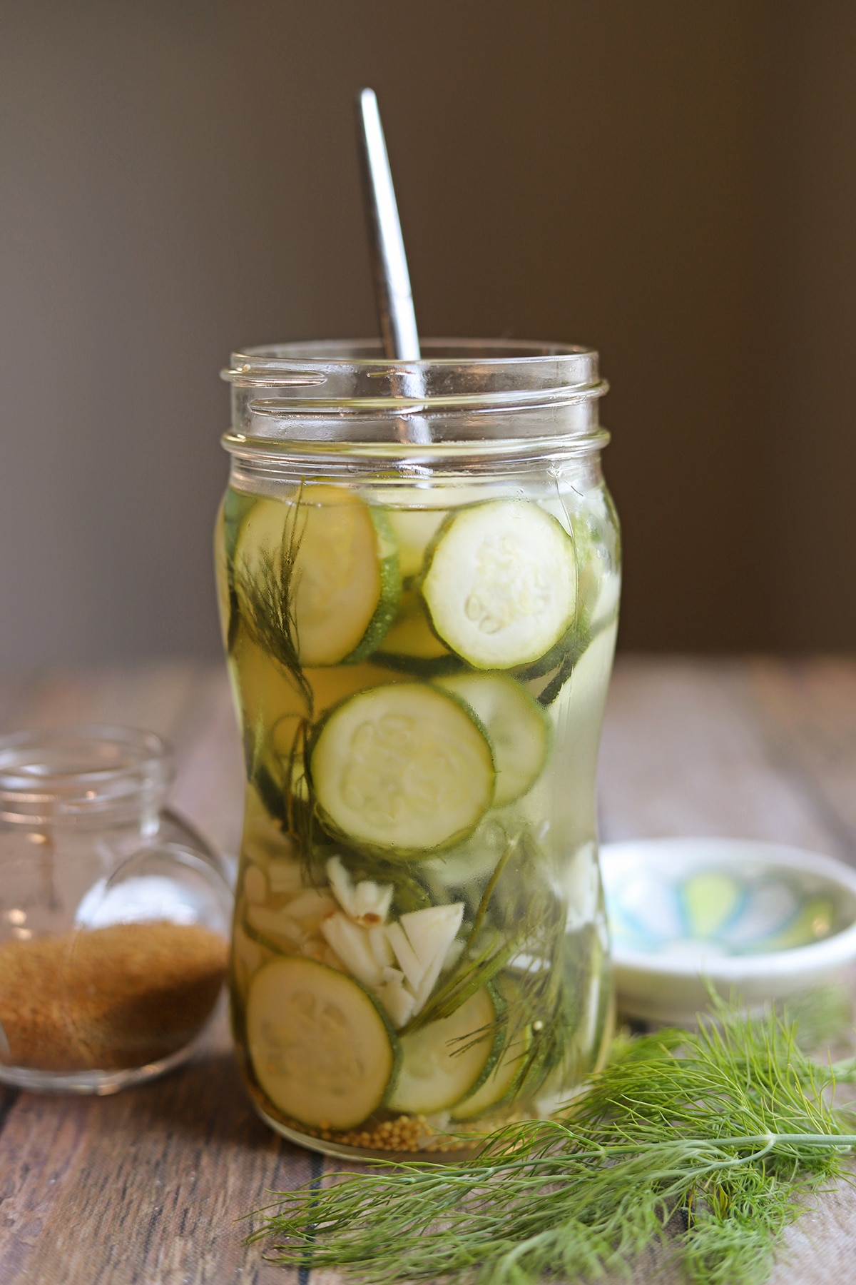 Thinly sliced pickled zucchini in jar with garlic, dill, and mustard seeds.