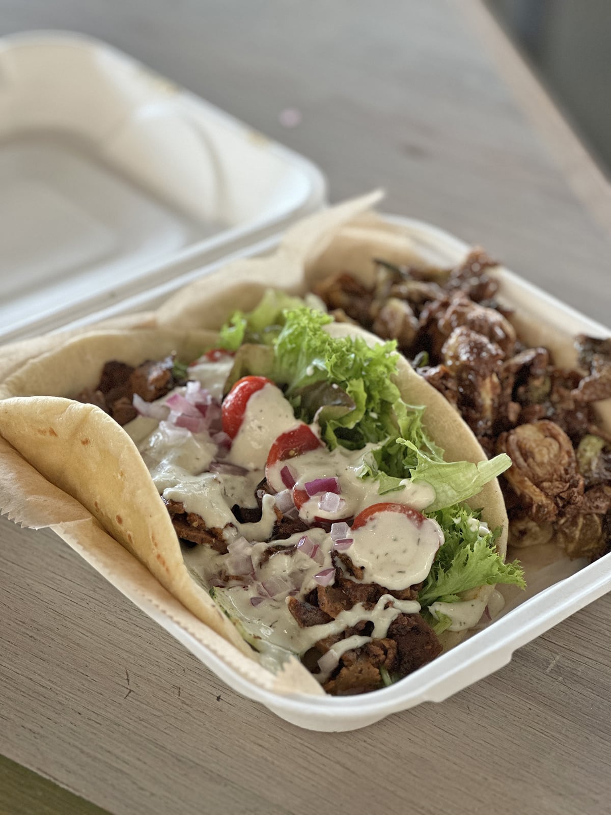 A vegan gyro with shaved seitan, greens, cucumber, tomato, diced onion, and tzatziki in a pita, plus a side of fried Brussels sprouts.