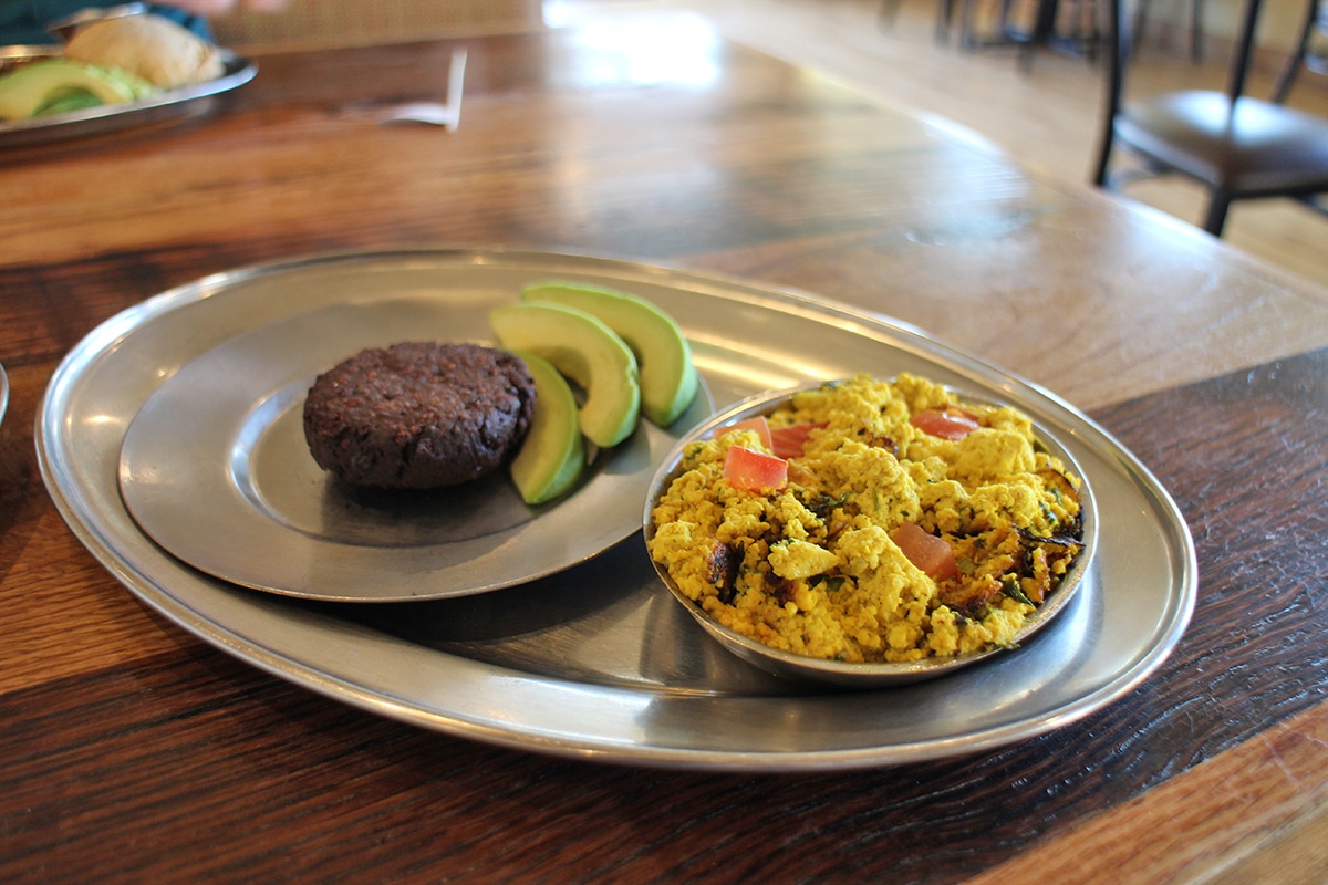Tofu scramble, veggie sausage, and sliced avocado on metal plate.