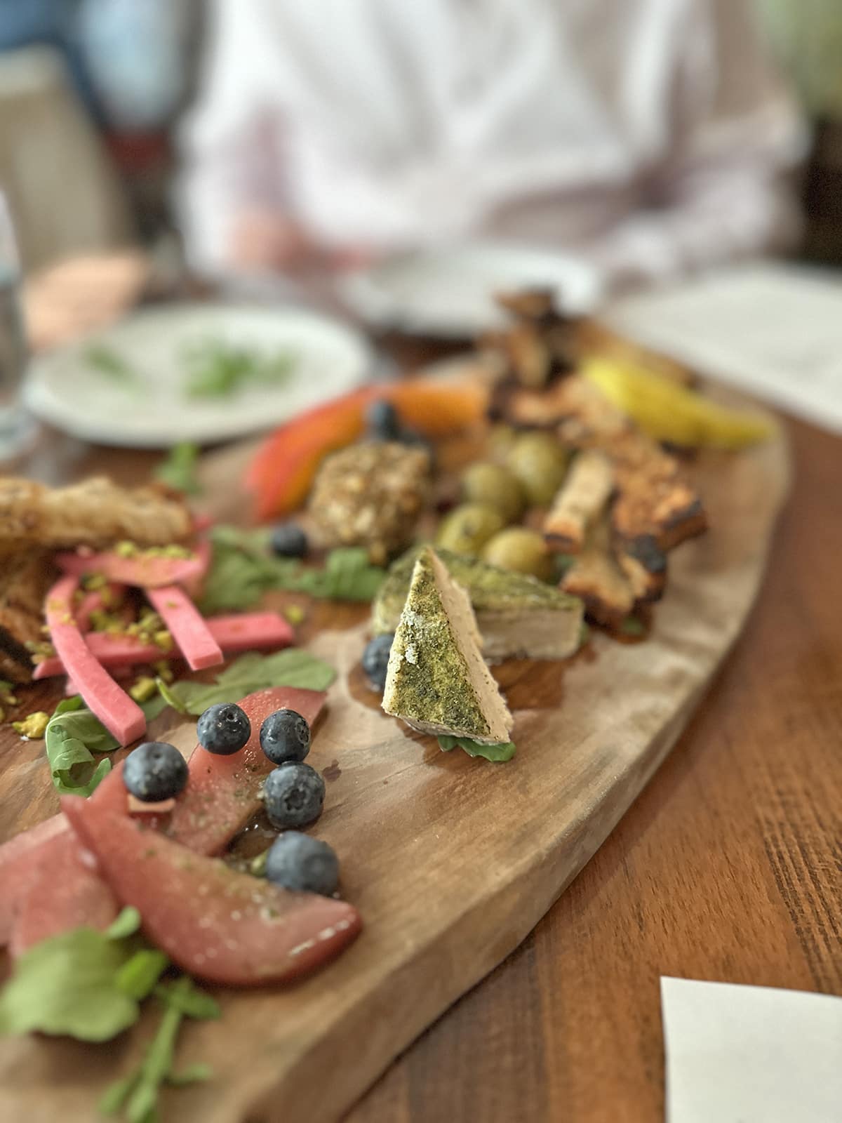 Aged cashew cheese on vegan cheese board with fruit and pickled veggies.