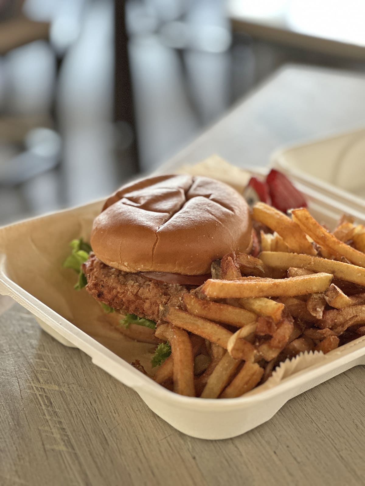 Vegan chicken sandwich with fries in to-go container.