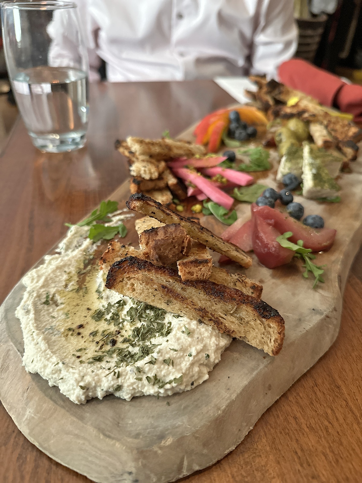 Vegan cheese board with non-dairy ricotta, toasted bread, pickled turnips, and blueberries.