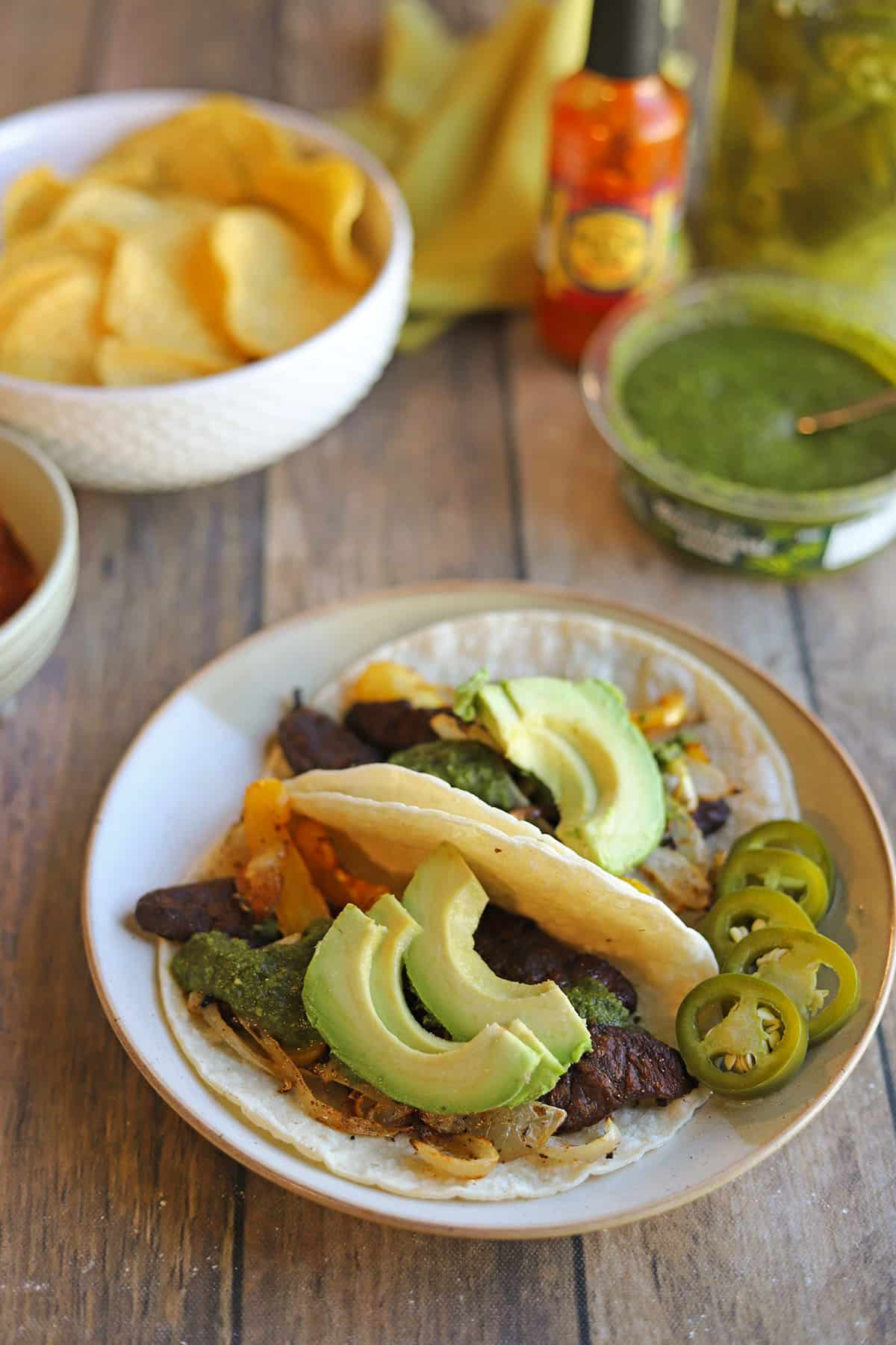 Beefless bulgogi fajitas on table with tortilla chips, chimichurri, and hot sauce.